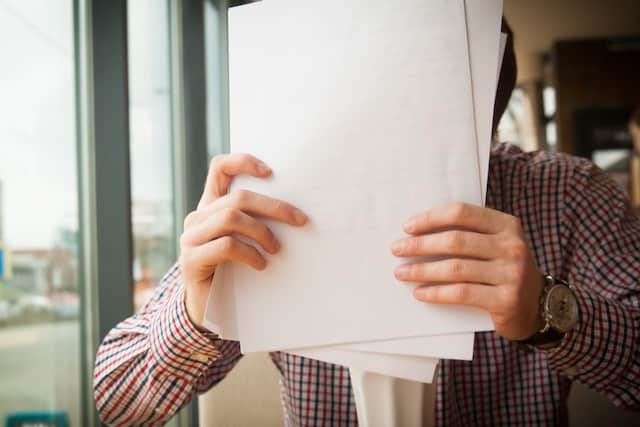 Mann hält Stapel Papier vor dem Gesicht