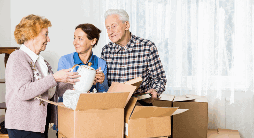 Senioren bei einem Umzug, eine Frau hilft einem älteren Paar beim Packen von Kartons und Verpacken von Erinnerungsstücken für den Umzug